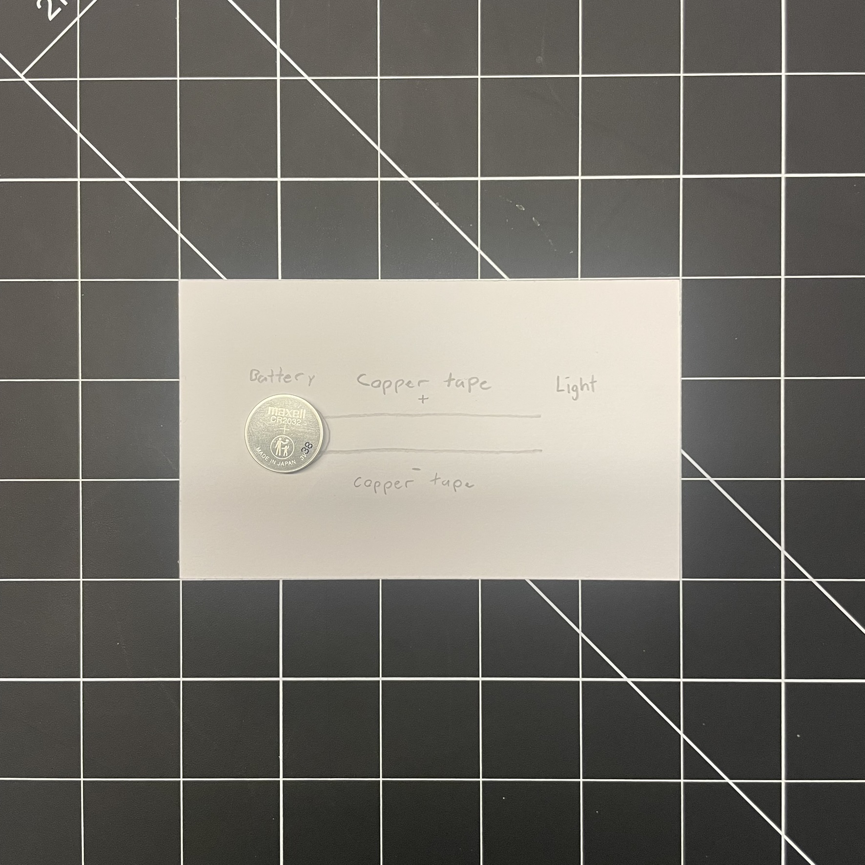 This is an image of the first circuit, the image contains a drawn outline/labels of the circuit along with the battery for it. The circuit is a basic positive and negative circuit that the tutorial video contained, with the copper tape acting as conductors between the light and the battery
